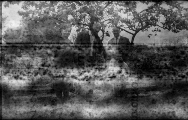 Very old black and white photo. Foggy and spotted, with markings from the backing paper showing, you can barely make out some people in old fashioned clothes and hairdos.