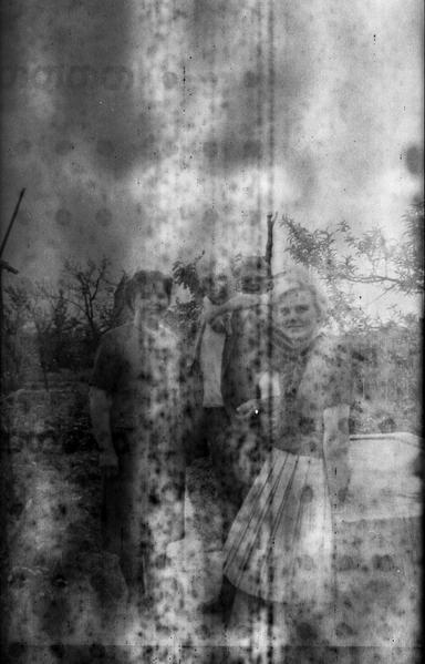 Very old black and white photo. Foggy and spotted, with markings from the backing paper showing, you can barely make out some people in old fashioned clothes and hairdos.