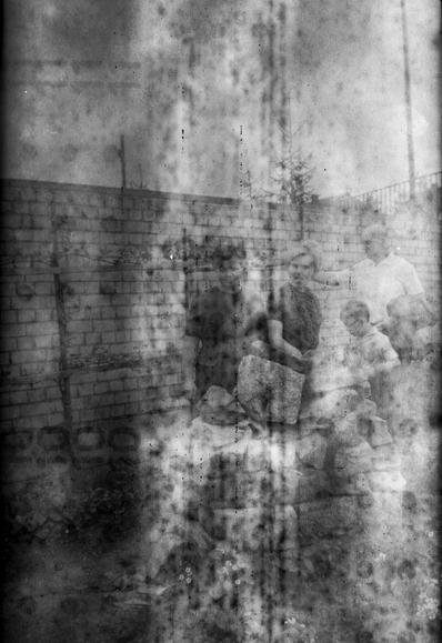 Very old black and white photo. Foggy and spotted, with markings from the backing paper showing, you can barely make out some people in old fashioned clothes and hairdos.