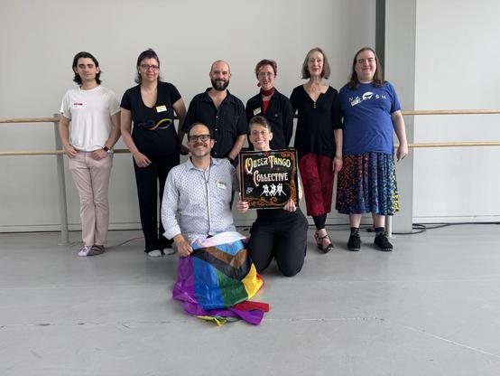 6 people stand while 2 in front hold a pride flag and a "queer tango collective" sign