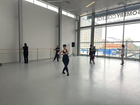 People walk around the dance floor with their arms held forward into big circles. One steps diagonally. Another extends a foot sideways.