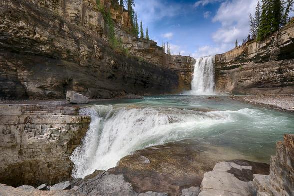 Crescent Falls in Alberta, Canada. Photographer POV: standing on the rocks at the edge of the pool, at the base of one waterfall, which serves as the top of the next cascading fall, which cascades out the bottom left side of the image.