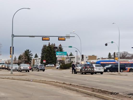 An intersection with two police cruisers with lights on, no traffic light working, automobiles stopped, and one SUV stopped in front of a police cruiser facing the wrong way, with the other side of the vehicle all smashed up.