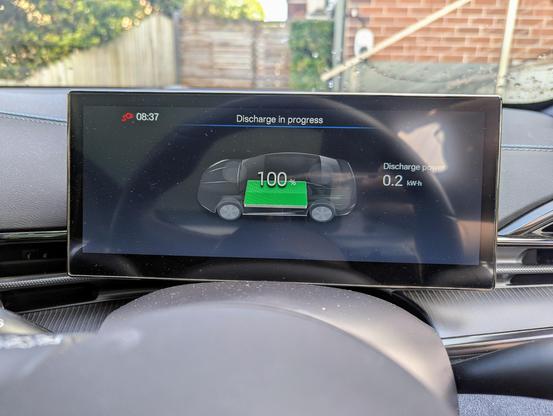 Photo of the driver's instrument display inside a BYD Seal electric car. It is showing the "Discharge in progress" screen, indicating that the car is being used to provide external mains power via the Vehicle to Load adapter. 0.2 kW of power is being used, and the battery is still at 100%.