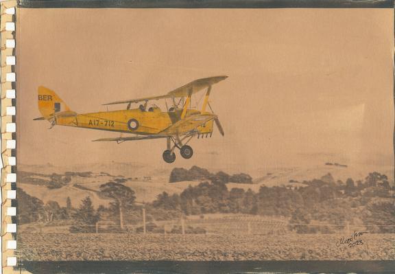 sepia toned print of Tiger Moth aircraft flying over low hills.