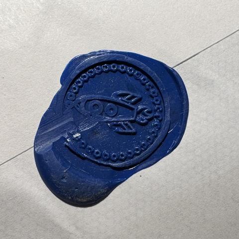 A blue wax seal on a white envelope. The seal is a little rocket!