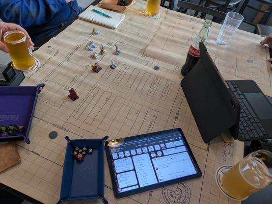 A dungeon map with several minis on it. There is a tablet open to a DnD Beyond character sheet, a dice tray, some beverages and many sets of polyhedral dice