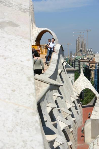 Tourists on the roof of Casa Milà in Barcelona with some Gaudi sculptures.
On the background the cathedral Sagrada Familia in scaffolding.