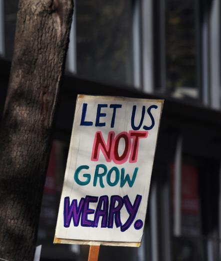LET US
NOT
GROW
WEARY
is written on a protest sign