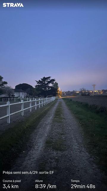 Un chemin de terre, bordé d’un côté par la barrière blanche d’un centre équestre et un champ de l’autre. Au loin, quelques arbres et à l’horizon un Château d’Eau, sous un ciel nocturne éclairé par le soleil levant. Des statistiques Strava sont visibles.