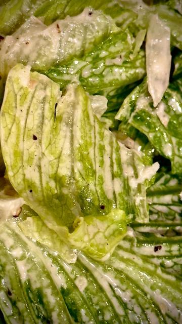 This is a close-up of a Caesar salad showing a few individual leaves coded with salad dressing between the veins of a leaf. There's this is Vangel amount of liquid there. If the leaves were not dry this would be diluted dressing instead of full strength.