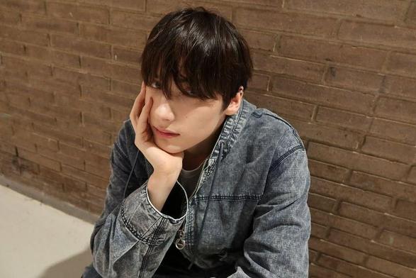 Kai backstage in Barcelona, wearing denim, posing in front of a brickwall