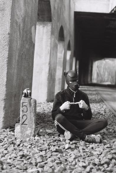 A Pup with fluffy hoodie and joggers sitting on cobblestone. Next to them, a millstone with a camera on it.