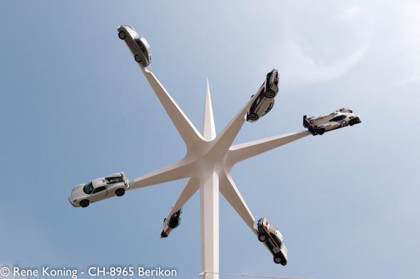 Das Bild zeigt eine große, weiße, sternförmige Struktur mit sechs Armen, die sich nach außen erstrecken. Jeder Arm trägt einen Porsche, der so positioniert ist, als würde er in der Luft schweben. Die Autos variieren in Design und Farbe, darunter eine silberne Limousine, ein weißer Sportwagen, ein schwarz-weißes Auto, ein weißes Auto mit roten Akzenten, ein silberner SUV und ein Polizeiauto. Der Hintergrund ist ein klarer blauer Himmel, der die Struktur und die Autos hervorhebt. Die Autos sind gleichmäßig um das Bauwerk herum angeordnet, so dass ein symmetrisches und visuell auffälliges Bild entsteht.

*** Übersetzt mit www.DeepL.com/Translator (kostenlose Version) ***
