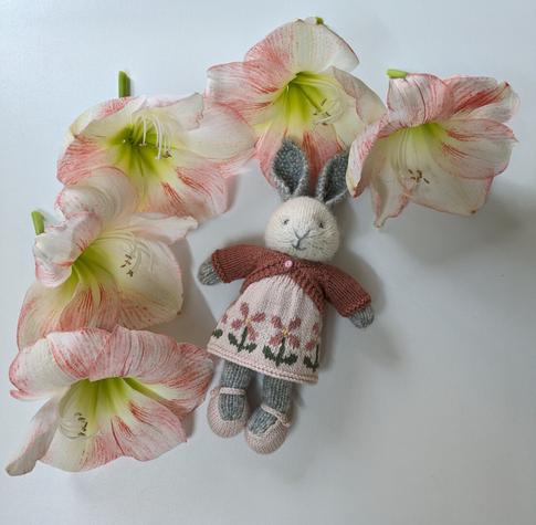 Small knitted rabbit wearing a pink cotton dress with a border of dark pink flowers and green leaves