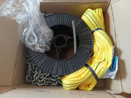 A cardboard box with a shipment from a commercial lifting equipment supplier. There's a yellow sling with rating sticker, two sizes of chain and a reel with 25m of flexible 10mm wire rope. Also some clamps and thimbles.