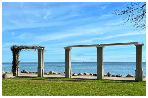 Blick durch zwei eckige Arkaden auf die blaue Ostsee unter strahlend blauem Himmel mit wenigen Schleierwolken. Im Hintergrund ein Schiff auf Reede