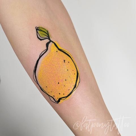 Tattoo einer Zitrone auf einem Unterarm. Das Motv ist kritzelig umrandet, die Farben schlicht und um ein Stück nach rechts versetzt.