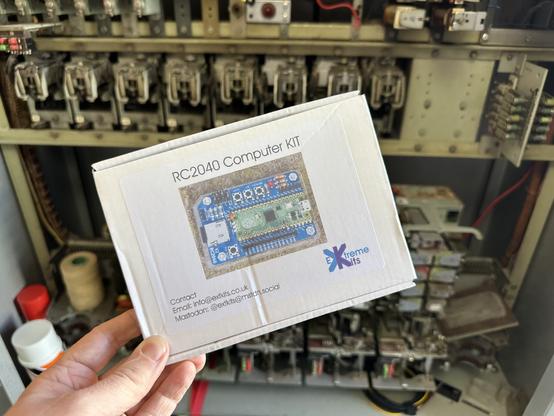 Hand holding a cardboard box with a picture of a circuit board on it. Titled “RC2040 Computer Kit” with the ExtremeKits logo and contact details