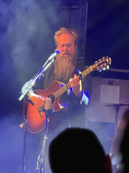 Closeup of Samuel Beam playing guitar with smoke behind him