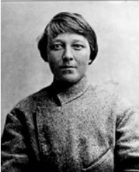 Maria Nikiforova, looking directly at the camera, not smiling, with short hair and wearing a sweater. Its origin unclear, this photo is believed to have been taken in Yelysavethrad (c. 1918). By Unknown author - Photo of the investigation file, Public Domain, https://commons.wikimedia.org/w/index.php?curid=9800753