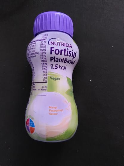 Small plastic bottle with purple lid mostly white with some green and leaves on bottom half. Text in large purple letters reads Nutricia Fortisip Plant Based 1.5kcal and in orange smaller letters Mango and Passion fruit Flavour. In very small purple letters is a list of ingredients.