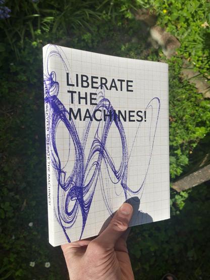 A hand holding up a (mockup) copy of the book "Liberate the Machines!" by Joost Rekveld.