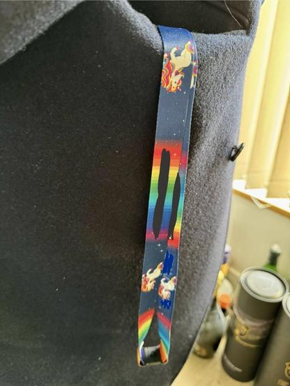 A dark coloured lanyard hanging out of a jacket pocket; with rainbows and unicorns (the company and department name have been censored).