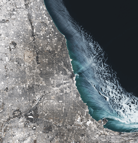 Satellite image of Chicago in winter. Fresh snow lies over the city and streaks of ice on the lake show winds pushing away from the shore.