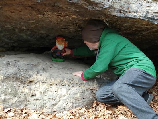 Großer Zwerg (Mensch mit grüner Jacke und Mütze) stellt die Figur Zwerg unter den Felsen.