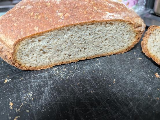 Ein angeschnittenes Brot auf einem schwarzen Brett, die Kruste ist mittelbraun, die Krume sehr feinporig