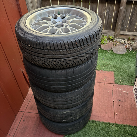 The five wheels and tires, including the full-size spare, removed from my 2003 BMW 5-series wagon (and donated by my former 2003 BMW 530i sedan) are stacked on my driveway, ready for the tires to be replaced. All of the tires except for the spare show significant tread wear.