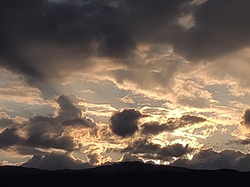 Ciel tourmenté, coins clairs mais nuages noirs, tout ça éclairé en orangé par le soleil qui vient juste de passer derrière la montagne
