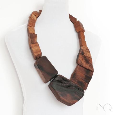En un maniquí blanco collar muy grande formado por trozos de madera grandes y sin pulir que parecen cada vez mas quemados según llegas a las piezas de mas abajo.