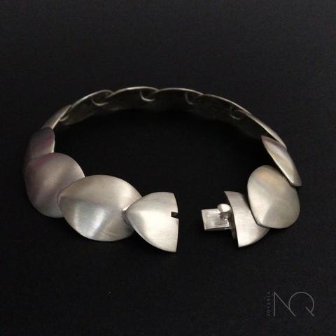 pulsera de plata con un acabado blanquecino y mate de laminas con forma de escamas abombadas que se montan unas encima de otras , la escama mas frontal esta  dividida para que se vea que esconde un mecanismo de cierre