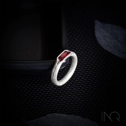 sobre fondo negro anillo de plata con lijado efecto mate y una banda brillante en el centro.
en la parte superior tiene una circonita de color rojo profundo y forma rectangular
