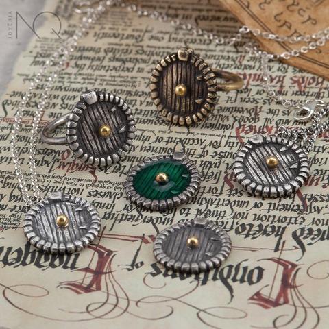 Sobre un pergamino medieval con letras caligraficas  hay anillos  y colgantes de plata que sumulan puertas hobbits redondeadas con pomos dorados