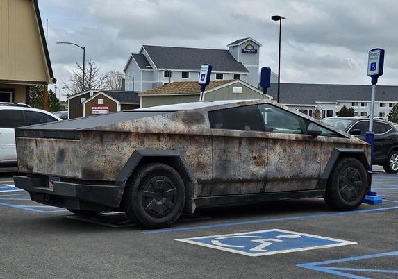 Badly corroded cyberdud with peeling panels and rust on every surface in a parking lot
