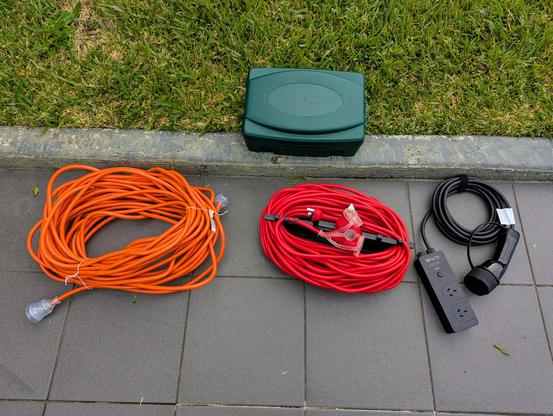 Photo of two very long mains extensions cables, a green box, and a V2L adaptor.