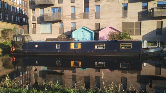 Dark blue barge with yellow window surrounds, reflecting in the evening waters of the Union Canal