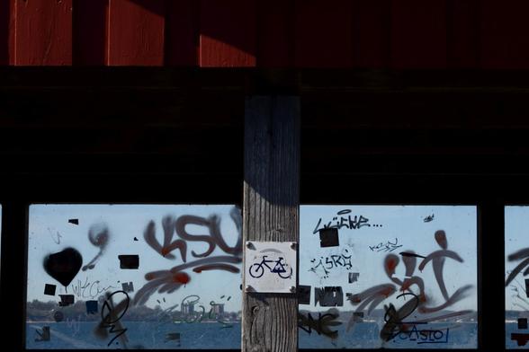 A bike sign at a ferry pier with a transparent back and a part of a red roof