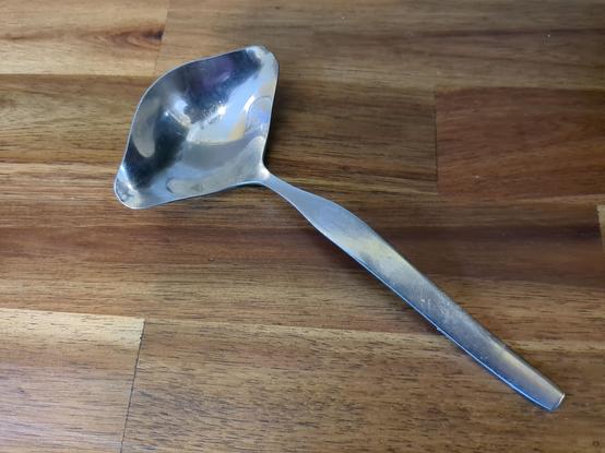 A metal spoon with a spout-like lip protruding on each side of the bowl.