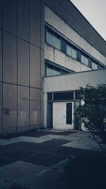 Socialist Modernism building facade. Doors locked, some windows broken. Tags written to a white door.