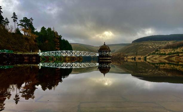 The pumping station at Tala reservoir reflected in an almost still water against a moody sky - just before a swim.