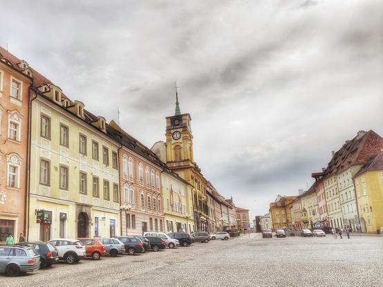 Im Zentrum der tschechischen Stadt Cheb. Links in der Mitte erhebt sich der Turm des Rathauses, rechts eine weitere Häuserzeile, die den Markt begrenzt. Der Himmel ist bewölkt.