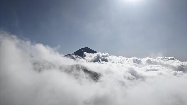 A mountaintop peaks above a dense layer of clouds.