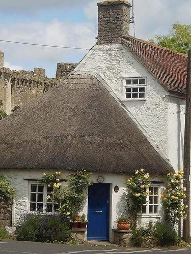 White property with a semi-circular thatched roof and a castle in the background.