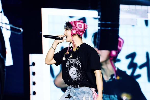 Han onstage during a concert. He's wearing a cute pink hat with earflaps, and has a light pink bandana attached to his left hip