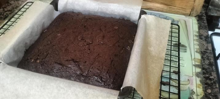 Chocolate fudge brownie fresh from the oven, still in it's tin, baking parchment over the sides to make it easy to lift out, and all on a black cooling rack