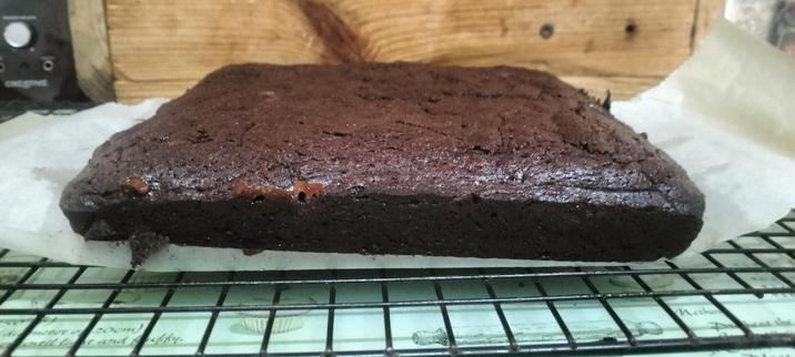 Chocolate brownie, still warm, out of its tin on the parchment sheet, on the cooling rack...some nice gooey fudge oozing from the side.